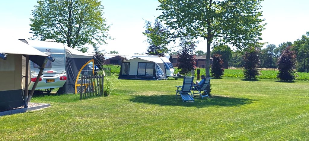 Caravan met voortent op een ruime grasplaats van een minicamping, met bomen en weiland op de achtergrond