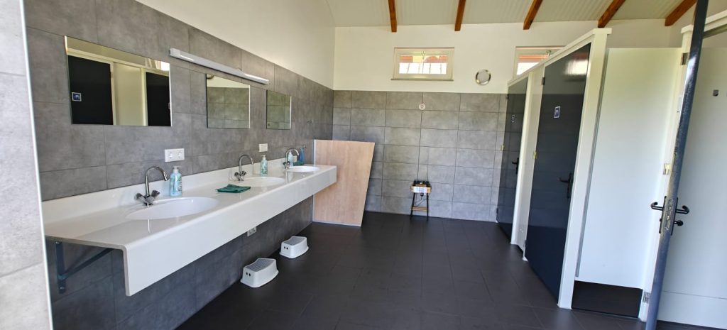 Modern sanitairgebouw met twee wastafels, spiegels en afzonderlijke doucheruimtes